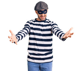 Young handsome man wearing burglar mask looking at the camera smiling with open arms for hug. cheerful expression embracing happiness.