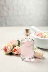 Fototapeta na wymiar Bottle of rose essential oil and flowers on white table