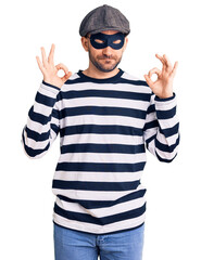 Naklejka premium Young handsome man wearing burglar mask relaxed and smiling with eyes closed doing meditation gesture with fingers. yoga concept.