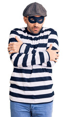 Young handsome man wearing burglar mask shaking and freezing for winter cold with sad and shock...