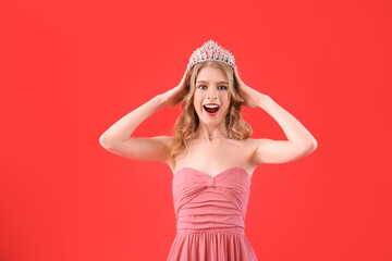 Surprised teenage girl in tiara and prom dress on red background © Pixel-Shot