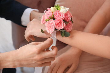 Teenage boy tying corsage around his girlfriend's wrist for prom in room, closeup - obrazy, fototapety, plakaty
