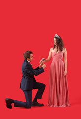 Young man tying corsage around his prom date's wrist on red background