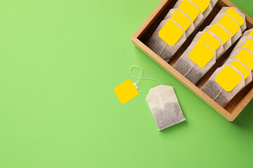 Many tea bags in wooden box on light green background, flat lay. Space for text