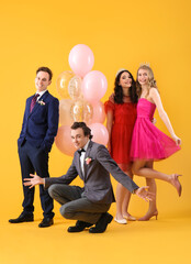 Beautiful couples dressed for prom with balloons on yellow background © Pixel-Shot