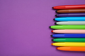 Fototapeta premium Different colorful markers on purple background, flat lay. Space for text