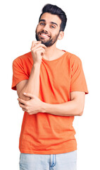 Young handsome man with beard wearing casual t-shirt looking confident at the camera smiling with crossed arms and hand raised on chin. thinking positive.