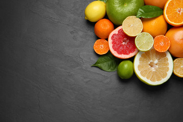 Different ripe citrus fruits with green leaves on black table, flat lay. Space for text