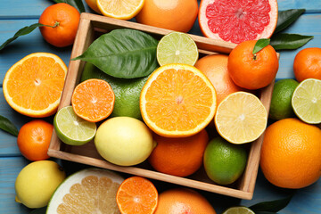 Different ripe citrus fruits with green leaves on light blue wooden table, flat lay