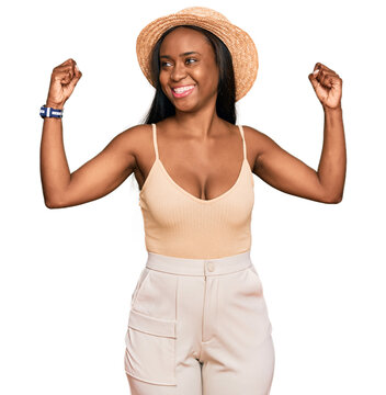 Young black woman wearing summer hat showing arms muscles smiling proud. fitness concept.