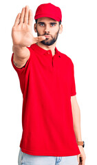 Young handsome man with beard wearing delivery uniform doing stop sing with palm of the hand. warning expression with negative and serious gesture on the face.