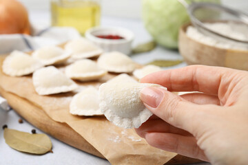 Woman holding raw dumpling (varenyk) with tasty filling at table, closeup