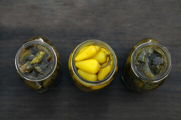 Glass jars of pickled green and yellow jalapeno peppers on wooden table, flat lay