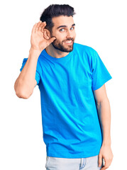 Fototapeta premium Young handsome man with beard wearing casual t-shirt smiling with hand over ear listening an hearing to rumor or gossip. deafness concept.