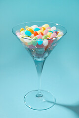 Beautiful martini glass with colorful candies on light blue background