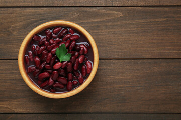Bowl of canned red kidney beans with parsley on wooden table, top view. Space for text