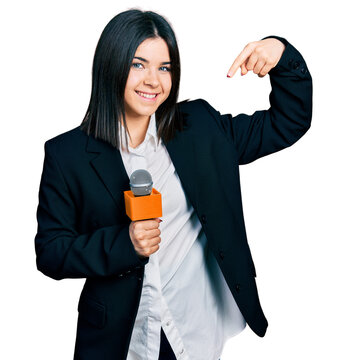 Young brunette woman with blue eyes holding reporter microphone pointing finger to one self smiling happy and proud
