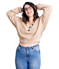 Beautiful young brunette woman wearing casual clothes and glasses relaxing and stretching, arms and hands behind head and neck smiling happy