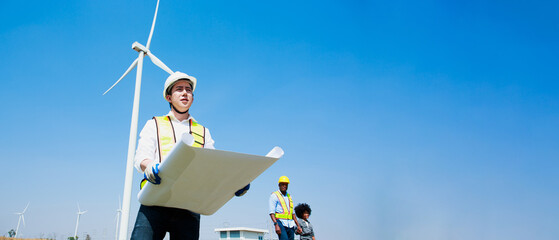 Asian engineer or architect working with his blueprints in hand while supervising construction site in Wind turbine farm power generator in beautiful nature landscape with copy space.