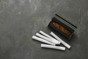 Roller with tobacco and hand rolled cigarettes on dark grey table, flat lay. Space for text