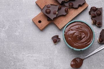 Chocolate pieces and bowl of sweet paste on grey table, flat lay. Space for text