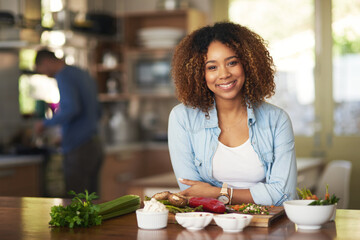 We like to keep our meals healthy. Portrait of a happy young woman preparing a healthy meal at home...