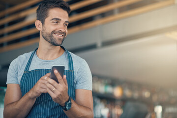 Smart baristas use the smartest tech. Shot of a young man using a mobile phone while working at a...