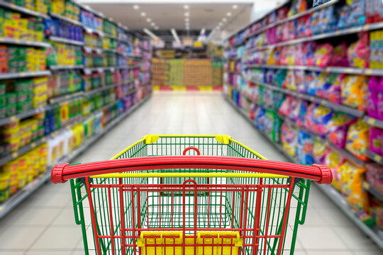 Supermarket aisle with empty shopping cart, blur background. Copy space.