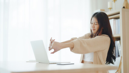 Fototapeta premium Office syndrome concept. Young asian woman feeling pain in neck and shoulder after working on computer laptop for a long time. She stretches to relax her muscles