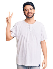 Young hispanic man wearing casual clothes smiling with happy face winking at the camera doing victory sign. number two.