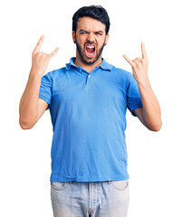 Naklejka premium Young hispanic man wearing casual clothes shouting with crazy expression doing rock symbol with hands up. music star. heavy concept.