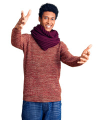 Young african american man wearing casual winter sweater and scarf looking at the camera smiling with open arms for hug. cheerful expression embracing happiness.