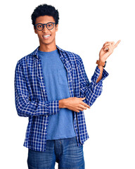 Young african american man wearing casual clothes and glasses with a big smile on face, pointing with hand and finger to the side looking at the camera.
