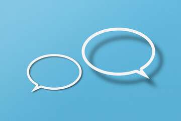 White paper cut out speech bubble shapes set on light blue paper background.