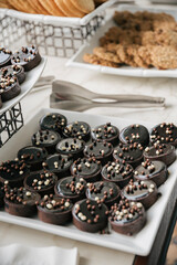 Platter of circular mini chocolate tarts on a table with tongs and plate of cookies in the background