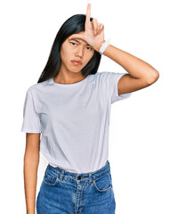 Fototapeta premium Beautiful young asian woman wearing casual white t shirt making fun of people with fingers on forehead doing loser gesture mocking and insulting.
