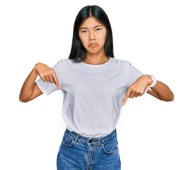 Beautiful young asian woman wearing casual white t shirt pointing down looking sad and upset,...