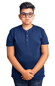 Little boy kid wearing casual clothes and glasses puffing cheeks with funny face. mouth inflated with air, crazy expression.