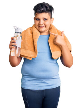 Little boy kid wearing sportswear drinking bottle of water smiling happy pointing with hand and finger
