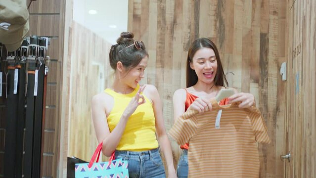 Asian young women holding hangers of clothes and entering fitting room