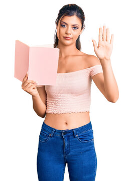 Young beautiful woman holding book with open hand doing stop sign with serious and confident expression, defense gesture