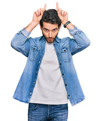 Young hispanic man wearing casual clothes doing funny gesture with finger over head as bull horns