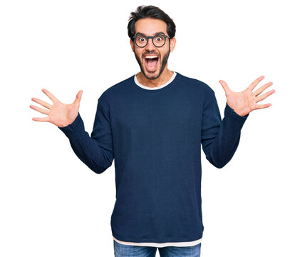 Young hispanic man wearing casual clothes and glasses celebrating crazy and amazed for success with arms raised and open eyes screaming excited. winner concept