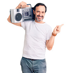 Middle age handsome man listening to music using vintage boombox smiling happy pointing with hand and finger to the side