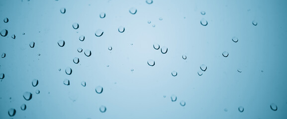 Minimal light backdrop with rain droplets on white glass. Light wet window with rainy drops closeup in blue light. Blurry minimalist monochrome background of window glass with raindrops close up.