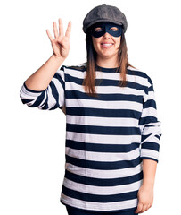 Young beautiful brunette woman wearing burglar mask showing and pointing up with fingers number four while smiling confident and happy.