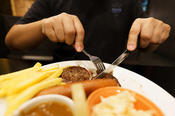 Man eating Grilled Meats stake from plate. hand holding knife and fork cutting grilled beef steak
