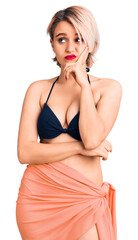 Fototapeta premium Young beautiful blonde woman wearing bikini serious face thinking about question with hand on chin, thoughtful about confusing idea