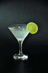 A glass of Margarita cocktail with ice and a slice of lime with a rim on a black background.