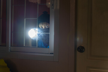 Thief Breaking House Window To Enter House.Burglar with flashlight looking through the window